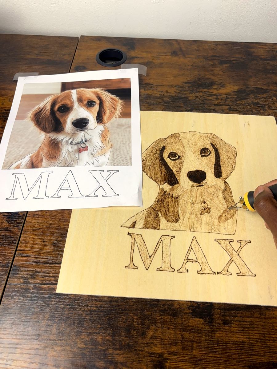 The completed portrait with a hand finishing the final stroke of the burned name lettering, freshly sealed